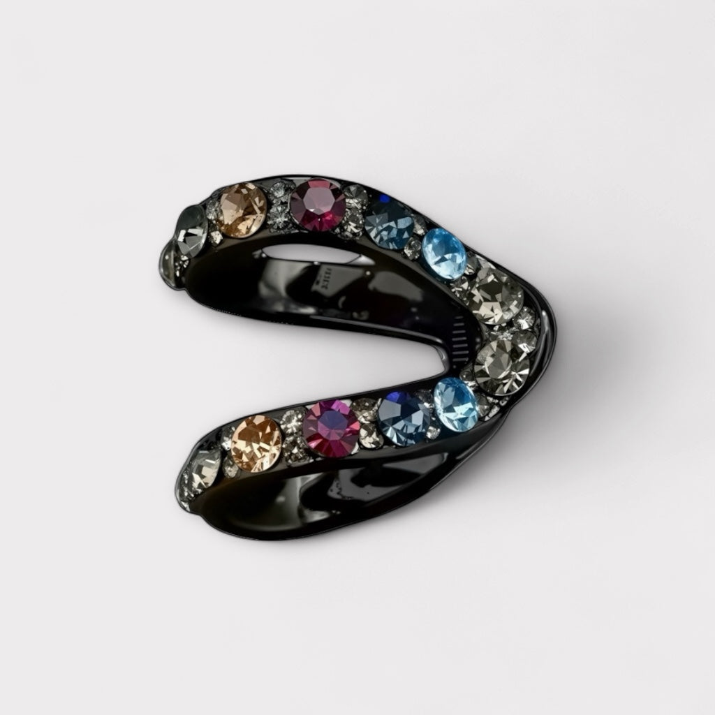 Close-up of crescent- shaped black hair claw clip with multicolored rhinestones in blue, rose, champagne and mint tones.