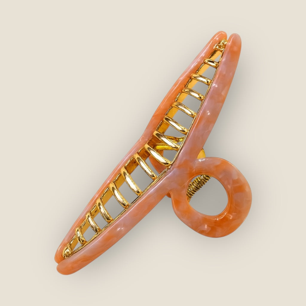 Glossy coral swirl hair claw with polished gold detailing display at an angle to slow depth and smooth finish.