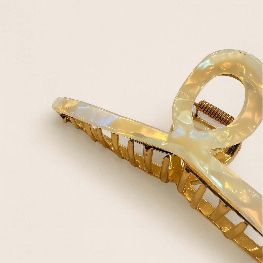 Close up of pearl effect sculpted hair clip with gold accents and shimmering acrylic loop handle.