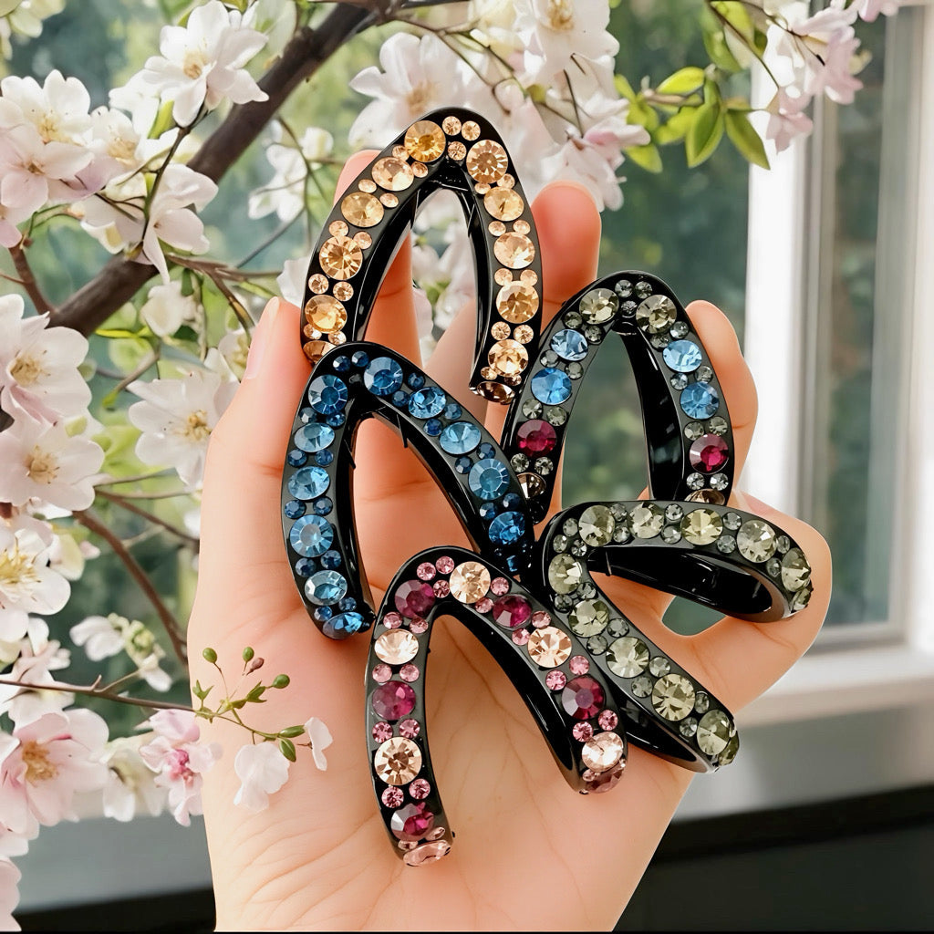 Hand holding five rhinestone crescent hair claws in assorted colors.