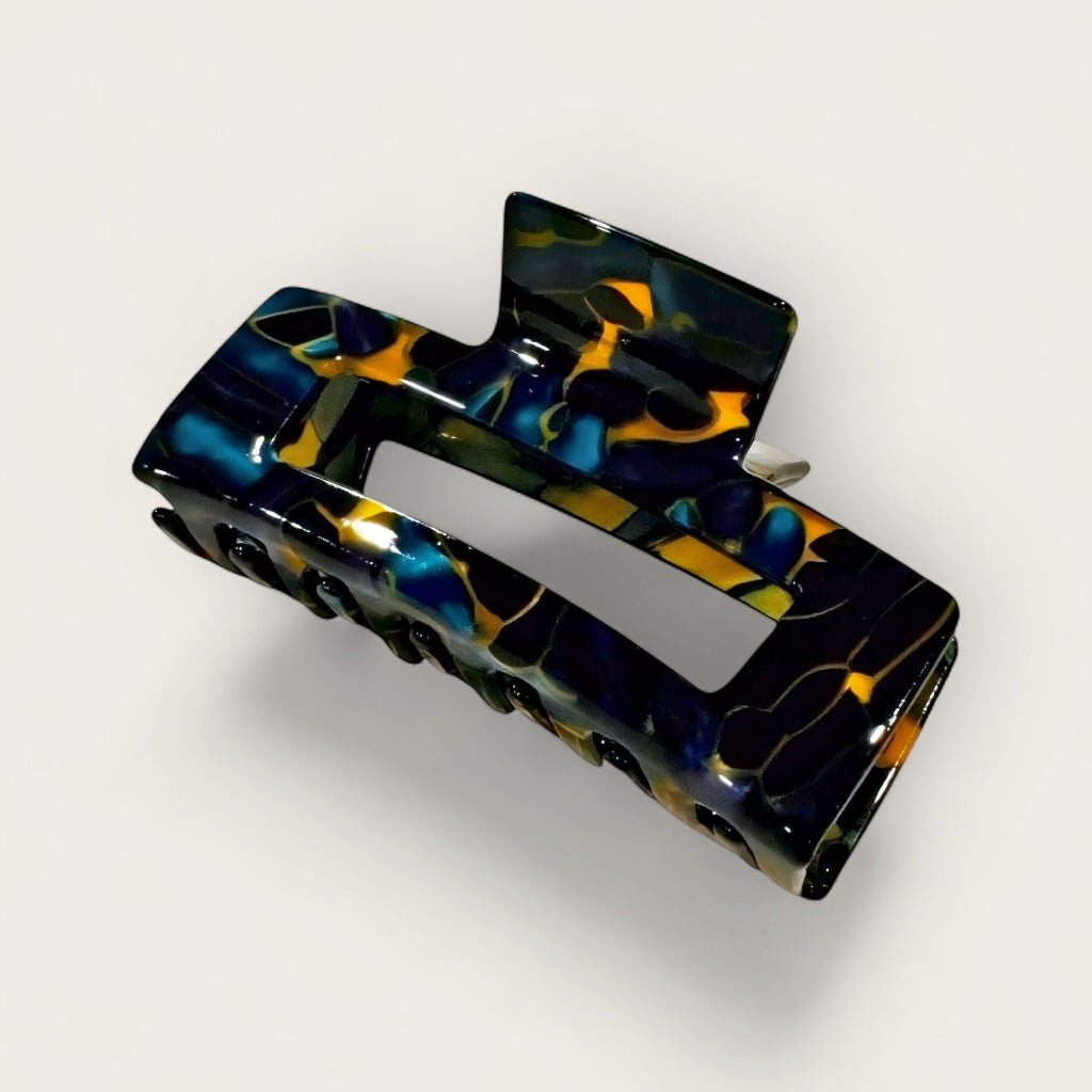 Ocean Noir hair claw clip in navy, amber, and black marbled resin on soft white, grey bckground.