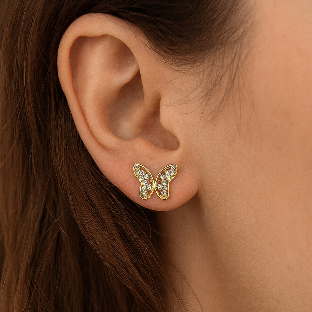 Close-up of PaulaB 14k gold plated butterfly earrings worn on ear, sparkling cubic zirconia accents.