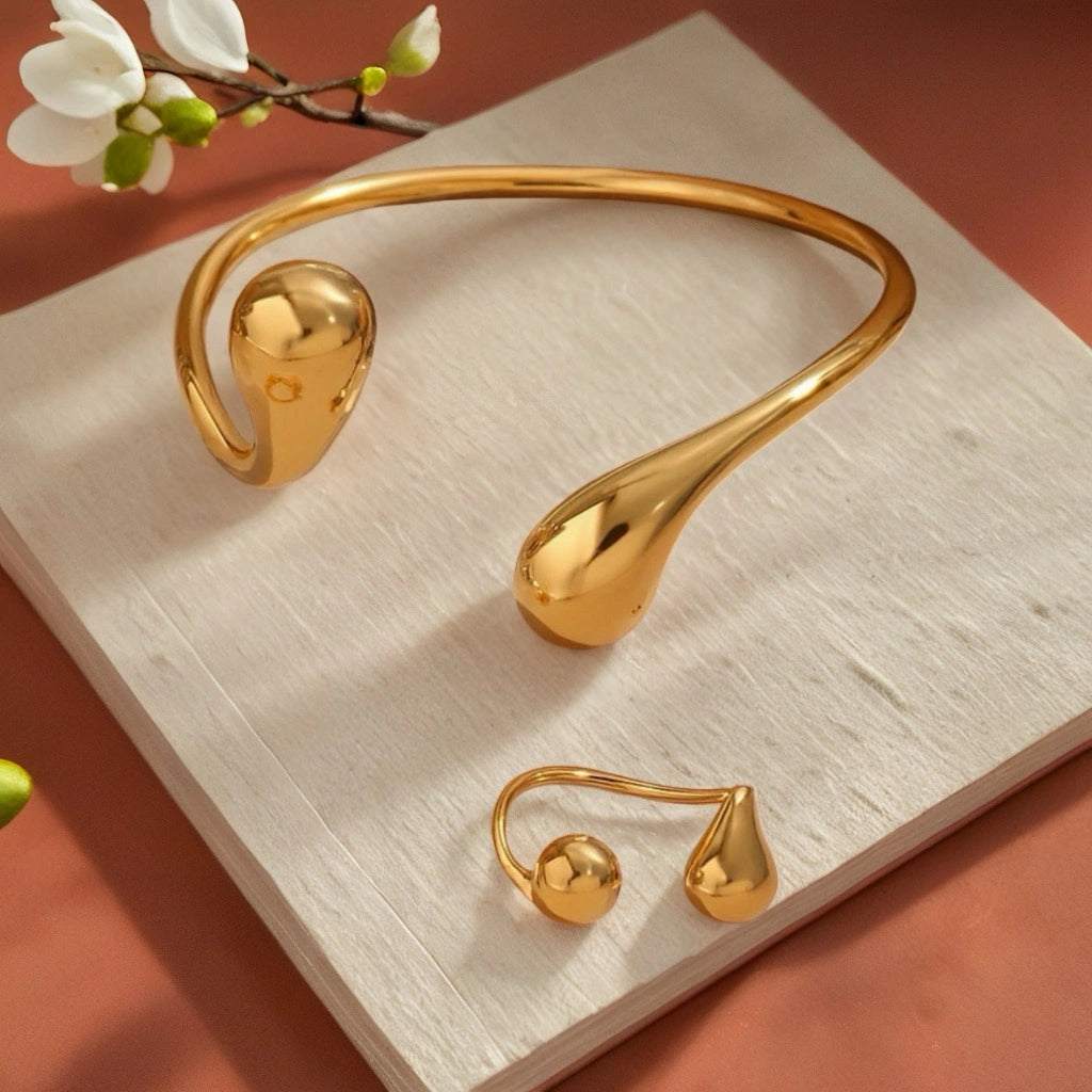 PaulaB Jewellery 18k gold cuff and matching ring flatlay on neutral background with floral accent, elegant minimalist design for Australian and New Zealand modern jewellery collections.