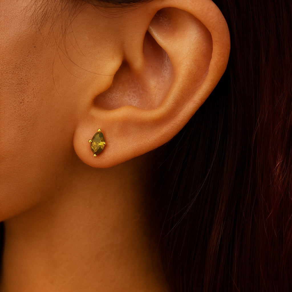 PaulaB 925 sterling silver stud earrings plated with 14k gold, featuring a marquise-cut green, emerald cubic stone, shown in a close-up on model's ear - Sydney, Australia.