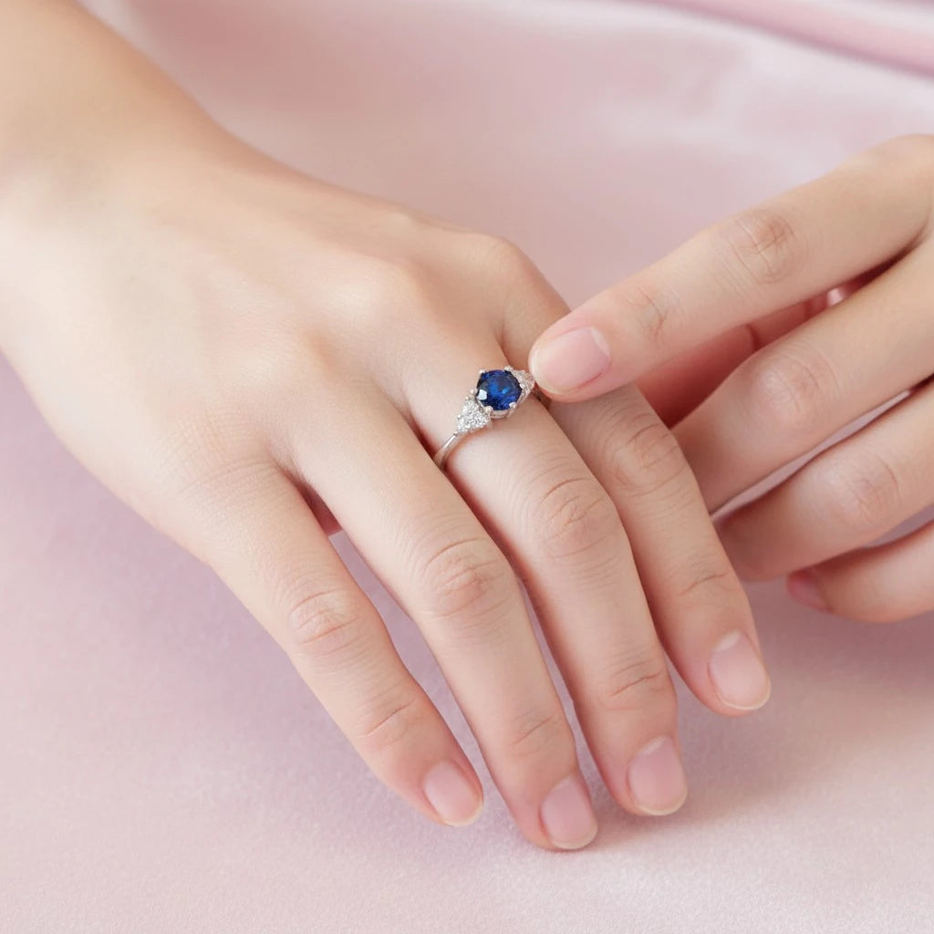 PaulaB rhodium plated sterling silver ring with deep blue sapphire shown in a soft pink lifestyle hand scene, adjustable fir ideal for Australia, New Zealand and UK buyers.