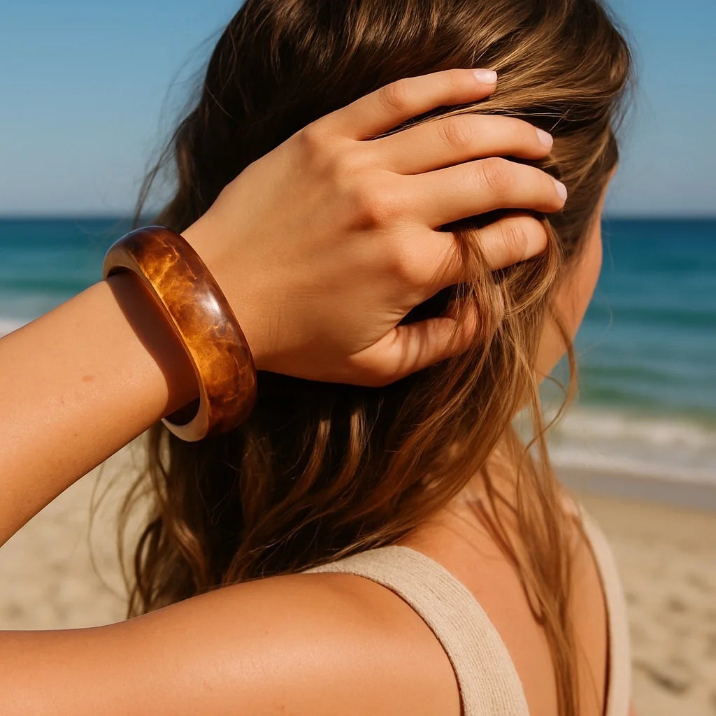 Model touching hair wearing PaulaB amber marbled bangle at the beach. Coastal lifestyle jewellery Australia, NZ, UK.