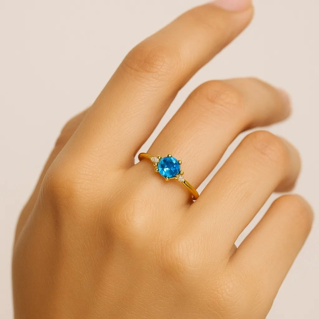 Close-up of adjustable gold ring with sparkling blue gemstone and diamond accents- PaulaB.