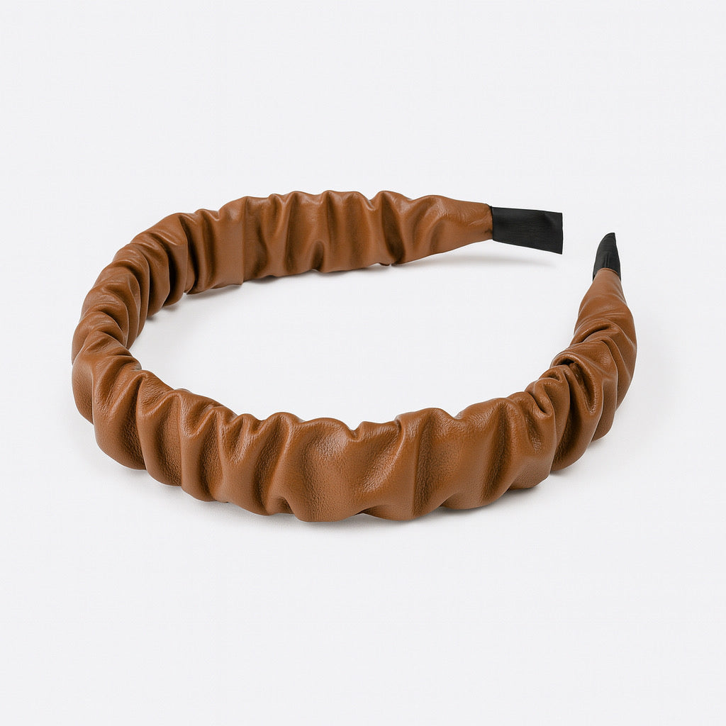 Flat lay of PaulaB brown faux leather ruched headband on white background for product display.