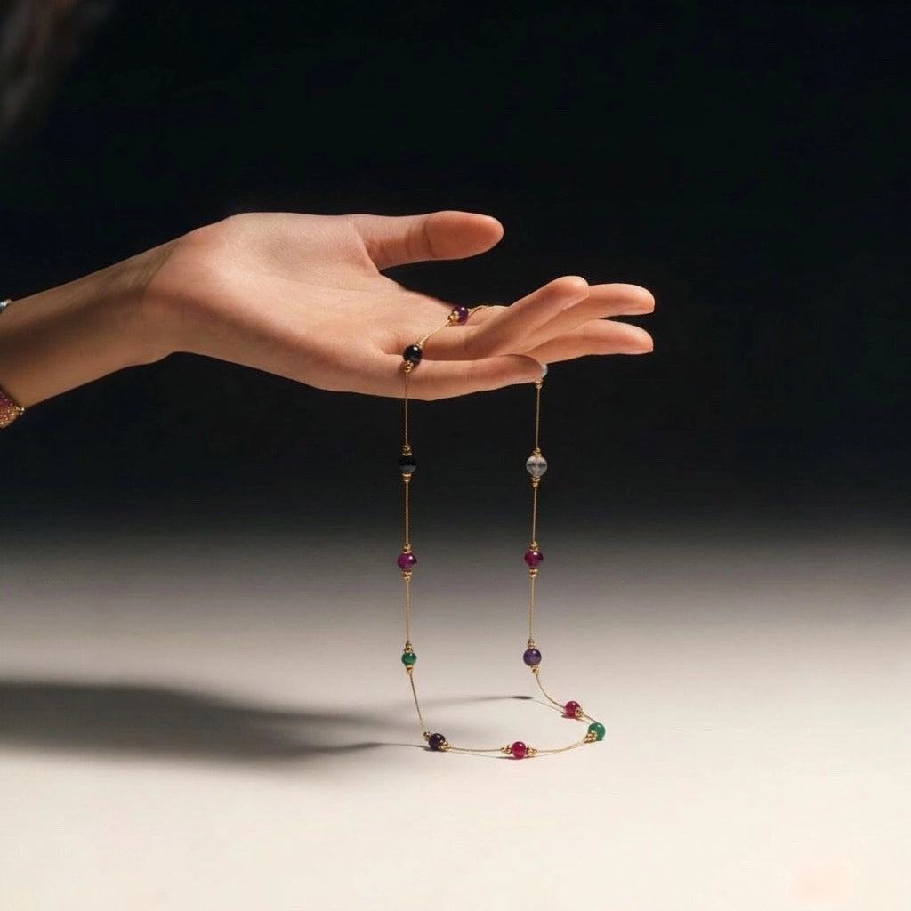 Elegant model holding PaulaB-gold-plated gemstone necklace in hand- artistic studio lighting luxury jewellery photo.