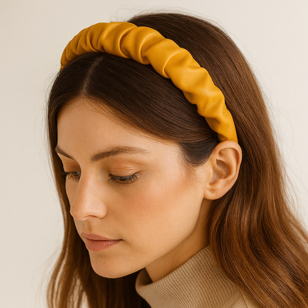 Model wearing Paula mustard yellow PU leather ruched headband in a close-up indoor view, showing elegant texture and soft shine. 