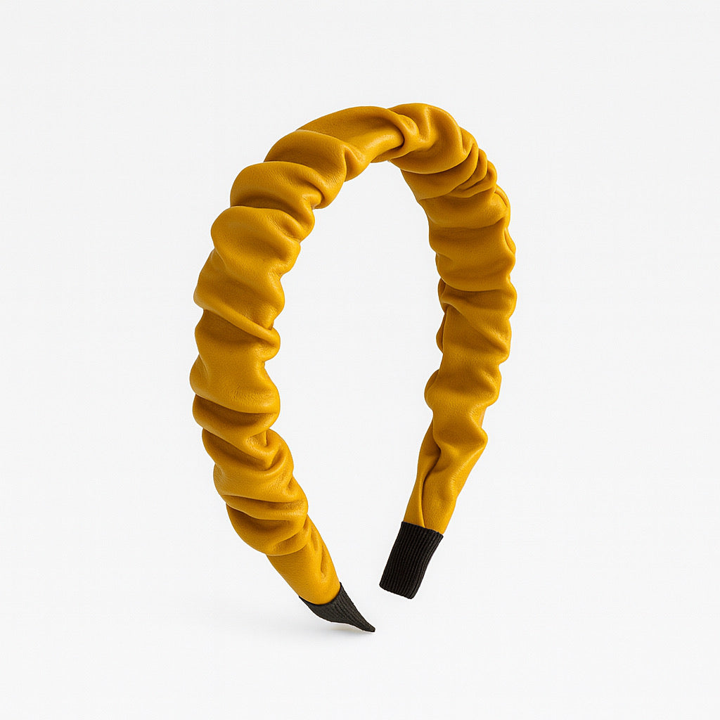 Mustard yellow PaulaB PU leather ruched headband standing upright on white background, with visible ruched folds and smooth PU finish