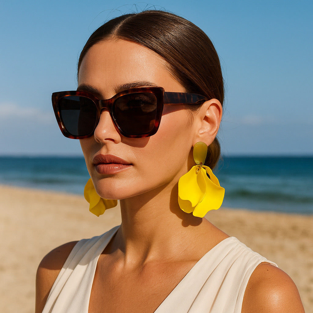 Model wearing yellow petal statement earrings at the beach with sunglasses.
