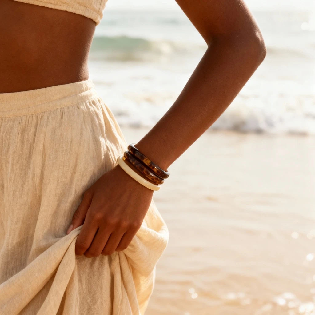 Editorial beach shot of PaulaB resin bangle stack, brown and cream bracelet set styled with linen skirt, jewellery for Australia NZ UK.