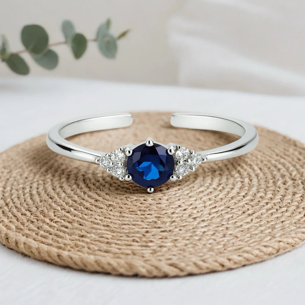 PaulaB rhodium plated sterling silver adjustable ring with dark blue sapphire on natural woven mat studio background. Premium jewellery for Australia, NZ AND UK customers.