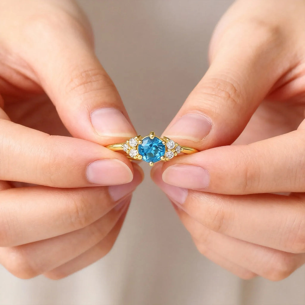 Close detail of hands holding gold ring with blue gemstone - PaulaB Jewellery handcrafted collection.
