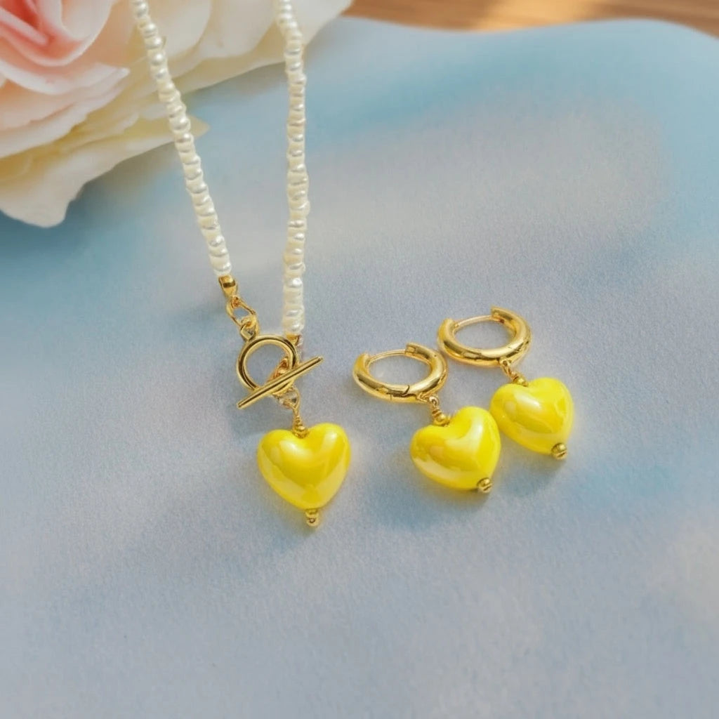 PaulaB Sunshine Yellow Heart Necklace and Earrings Set flat lay with glossy pearls and 14k gold finish on blue pastel surface, feminine fashion accessories New Zealand. 