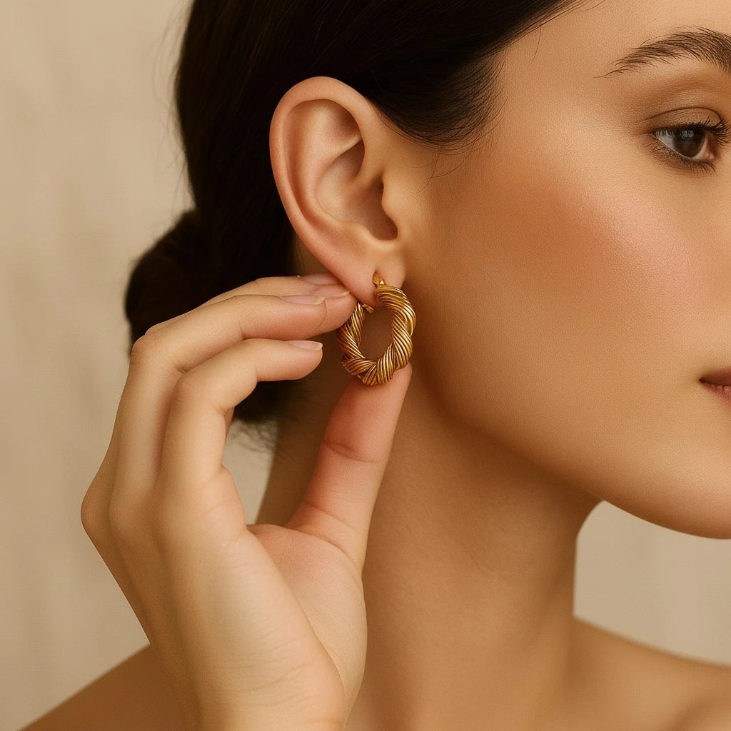 Close-up of PaulaB Twisted 18k gold-plated hoop earrings held by model, luxury copper base, polished gold tone, modern romantic jewellery photographed for PaulaB Australia, New Zealand & UK.