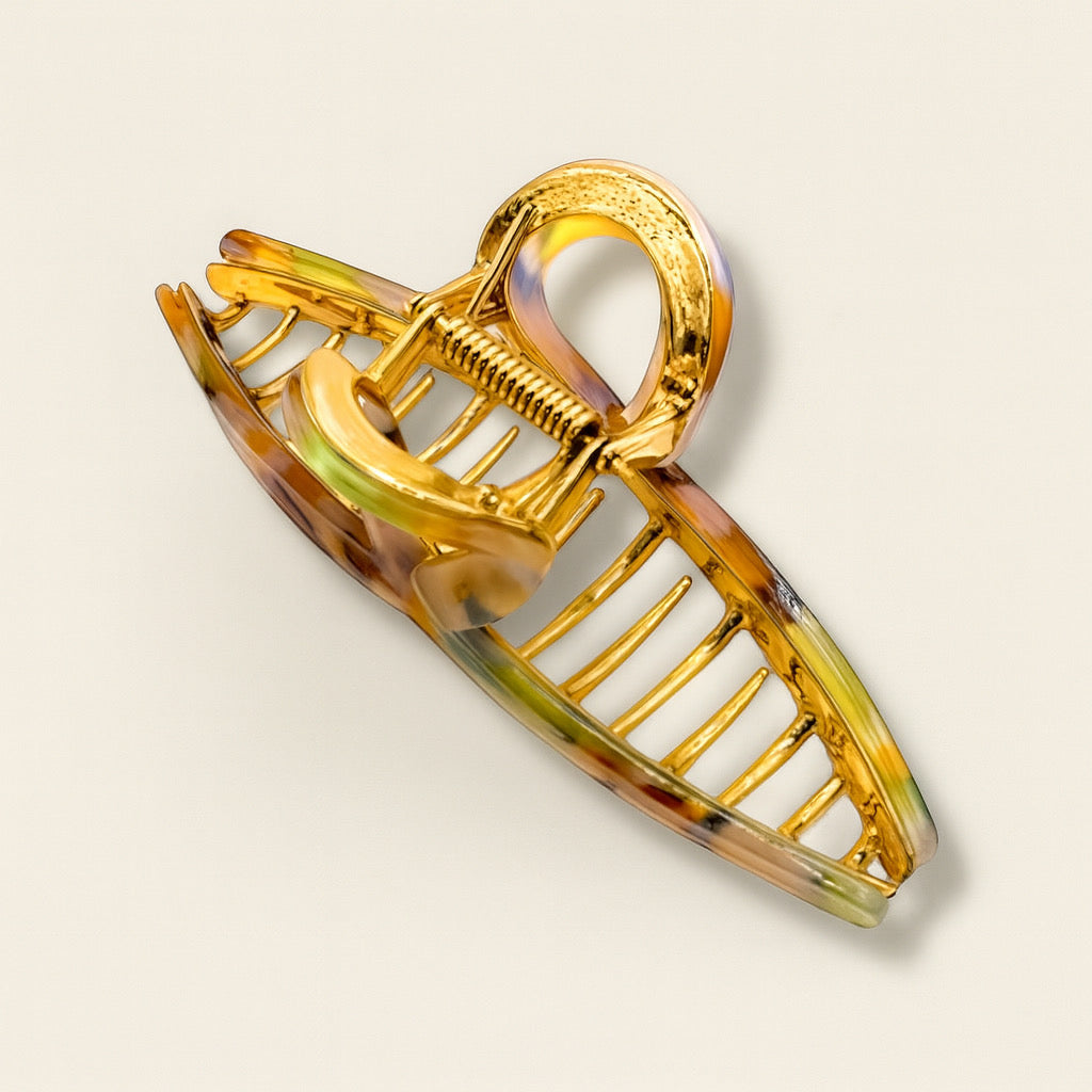 Close up of sculptural multicolor marble hair claw clip with polished gold prongs, placed on warm peach backdrop.
